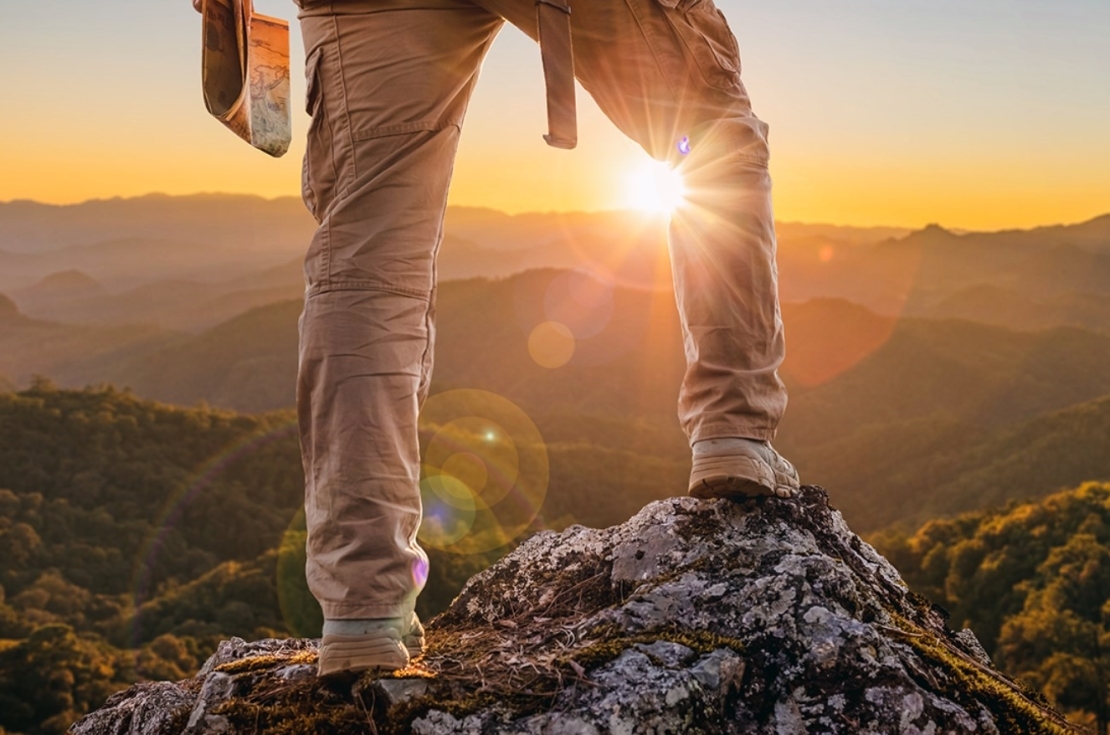 Close view of man at top of mountain looking down at sunset.